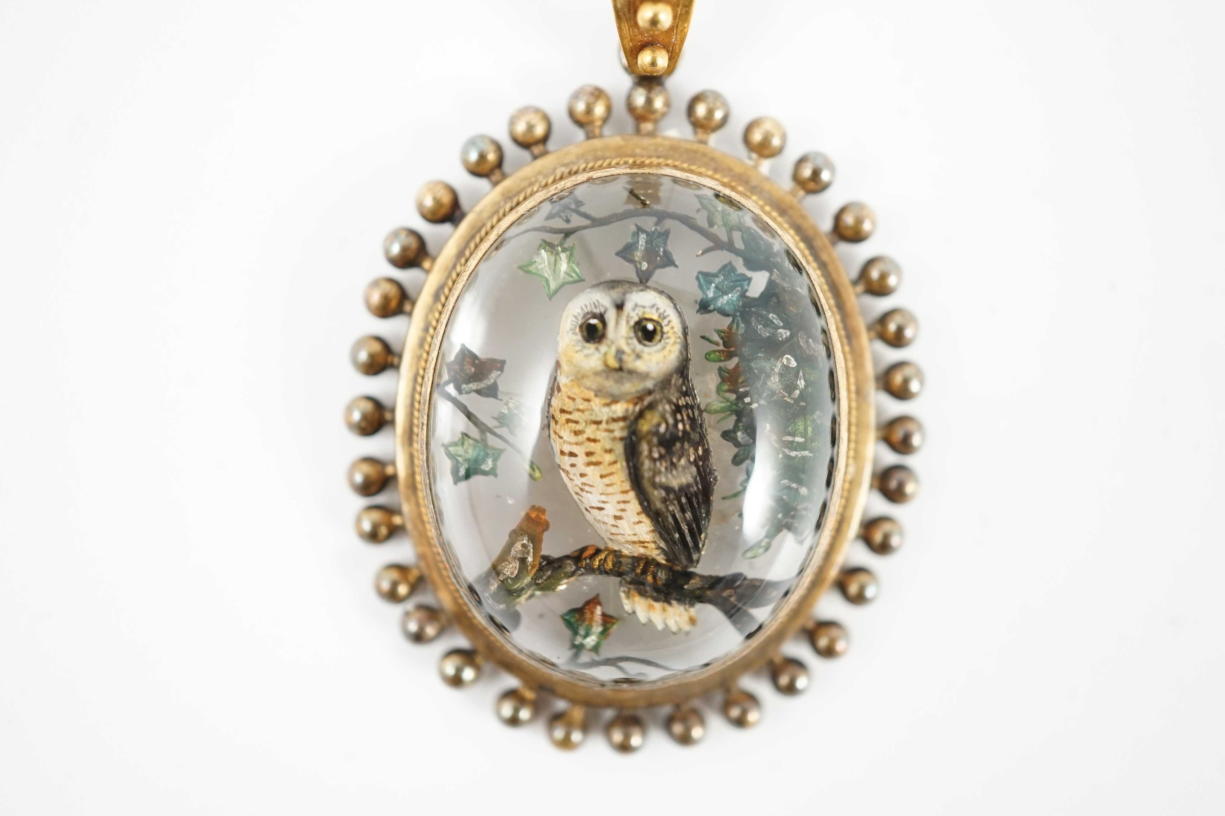 A Victorian yellow metal mounted Essex crystal oval pendant, depicting an owl upon a branch, amid foliage